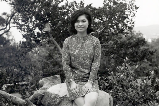 An undated black and white photo of Jenny Rose Ng sitting on a rock outside.