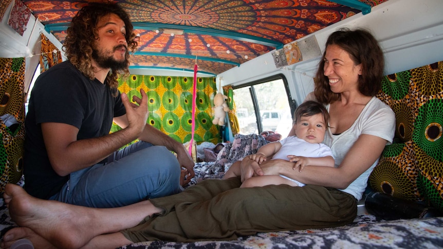 A man, woman and baby in the back of a van. walls covered in decorative cloth.