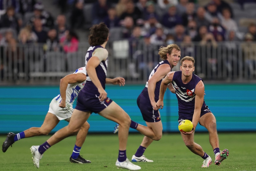 A Fremantle AFL player bends low as he gets ready to send a sweeping handball wide to a running teammate.