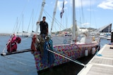 A woman stands on the bow of a yacht moored in a marina.