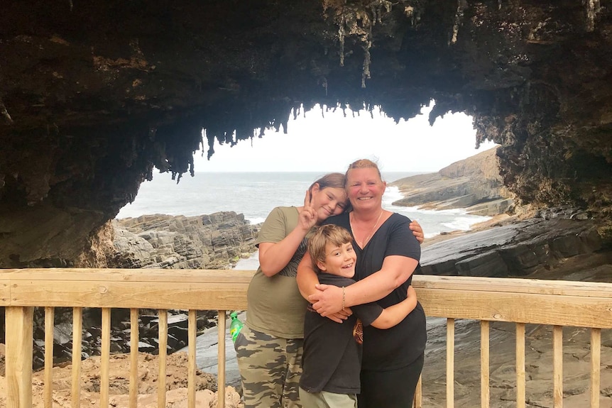 A woman and her young sons pose for a photo in front of a coastal rock formation.