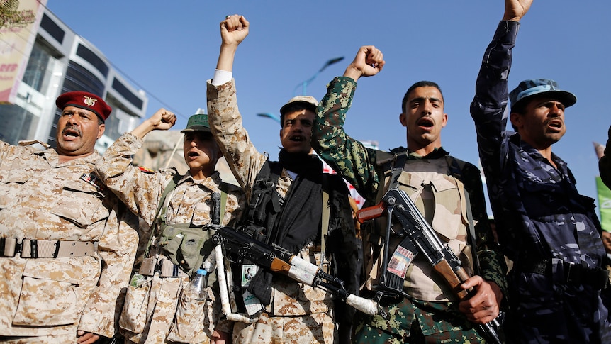 A row of men with guns holding their fists up as they chant