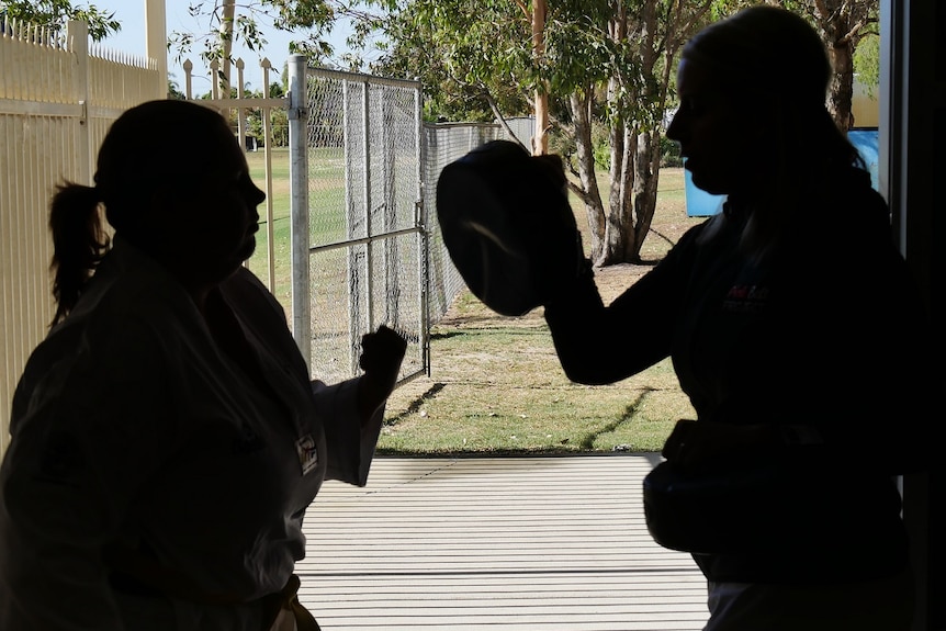 Silhouettes of a woman punching and another holding a pad