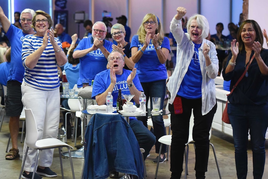 People wearing blue Democrat shirts clap and punch the air