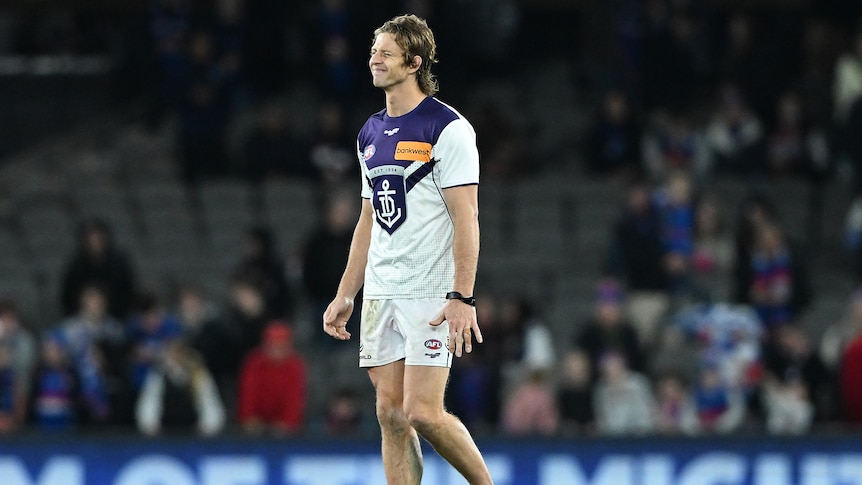 Nat Fyfe walks on the field with one shoe on wearing a pained expression