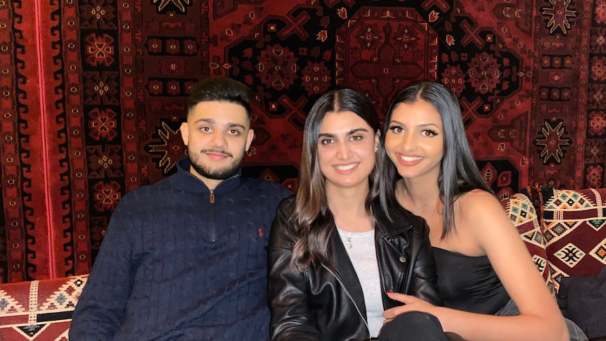 Three young Afghan Australian adults with a red rug in the background.