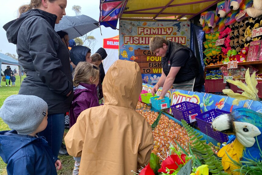 A group of children standing in front of a sideshow attraction fishing game. 