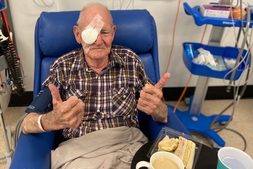 A man in a recovery chair in a hospital ward, one eye bandaged after eye surgery