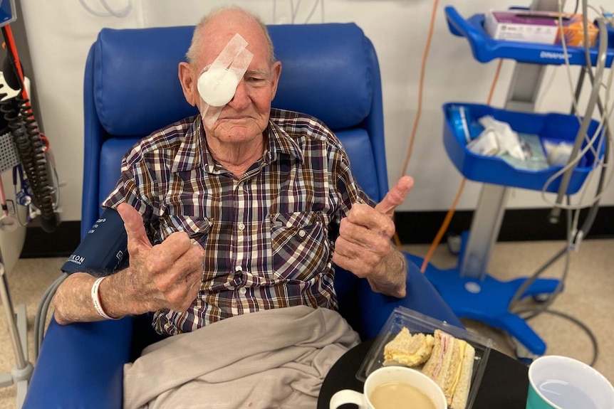 A man in a recovery chair in a hospital ward, one eye bandaged after eye surgery