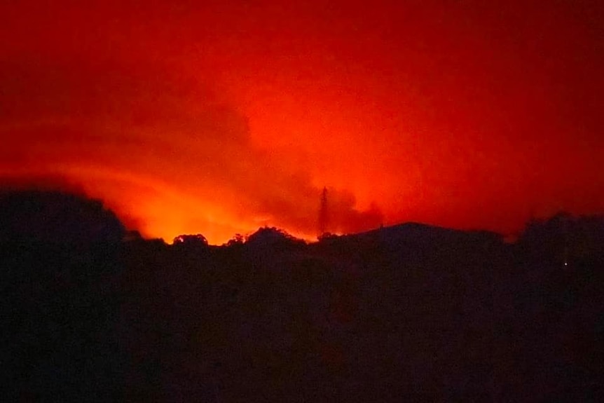 The sky is red-orange over the silhouetted roofs of a small town.