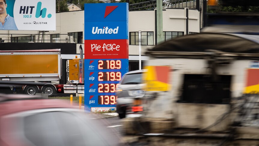 Petrol prices on a board with blurred traffic driving in front 
