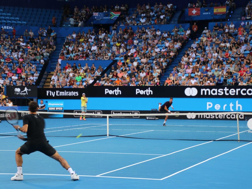 Federer hits the ball over the net, one leg up in the air.