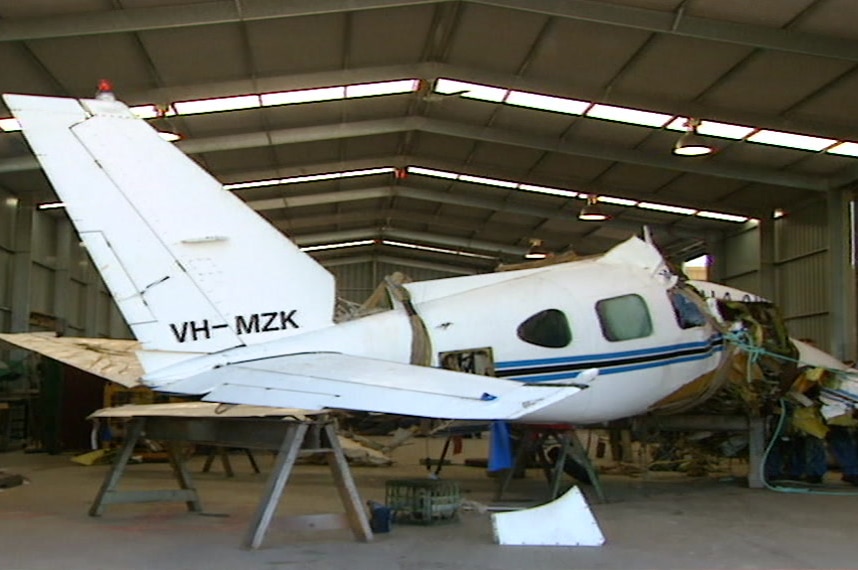 The wreckage of a plane inside a large shed. The front of the plane is missing.