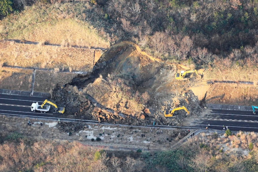 An aerial view of a barren highway blocked by a pile of rock as a truck carries out repairs.