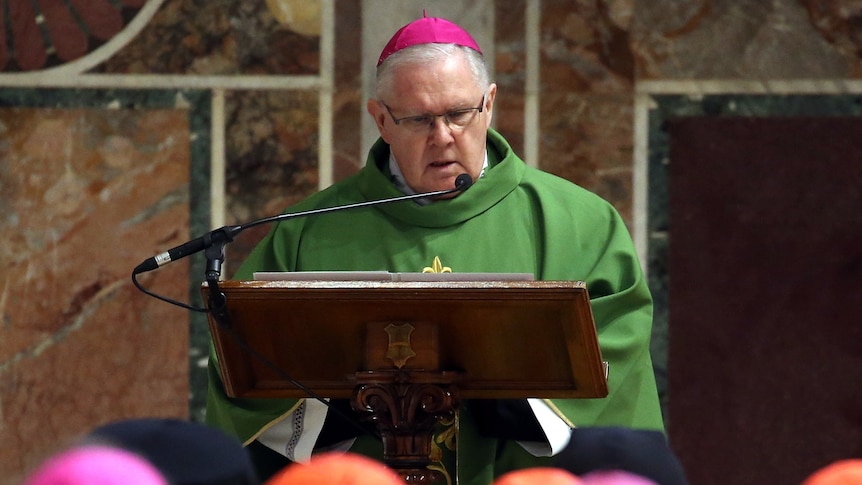 Mark Coleridge speaking in front of lectern wearing green robes and pink zucchetto