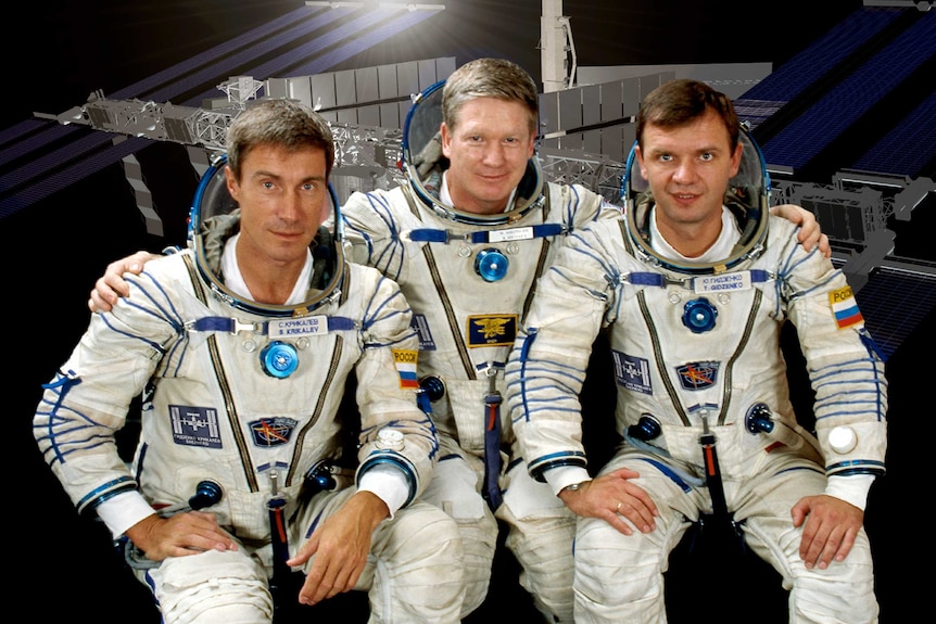 Three astronauts pose for a photo in their space suits