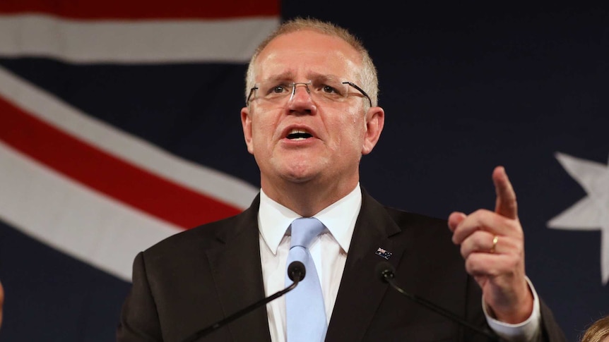 Prime Minister Scott Morrison gestures during a speech claiming victory in the federal election in front of the Australian flag.
