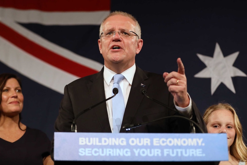 Prime Minister Scott Morrison gestures during a speech claiming victory in the federal election in front of the Australian flag.