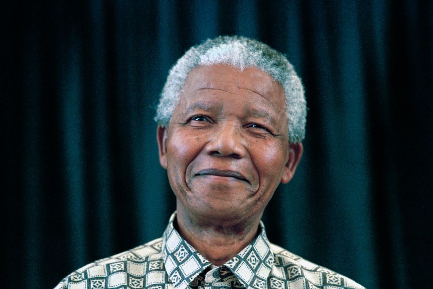 Close-up image of Nelson Mandela, with white-grey hair, smiling widely and looking ahead.