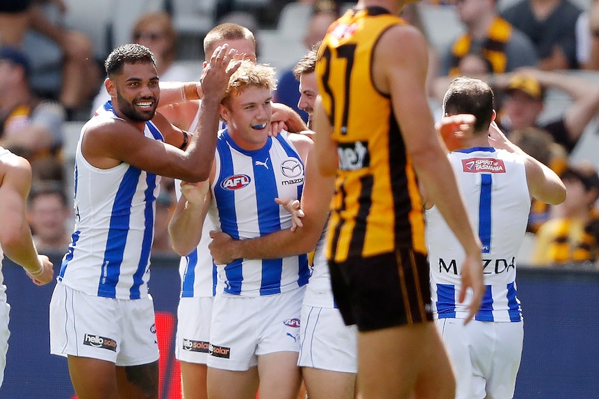 AFL players rub a teammates head and hug him after his goal during a game.