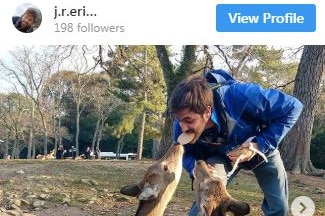Instagram post showing a man leaning over and feeding deer with a cracker in his mouth.