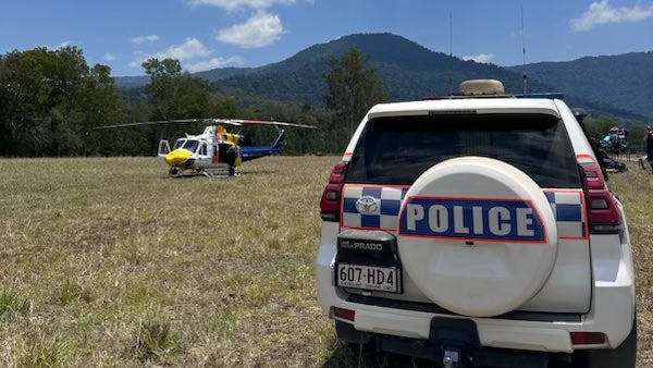 A police vehicle and a rescue helicopter on grass with mountain in the background.