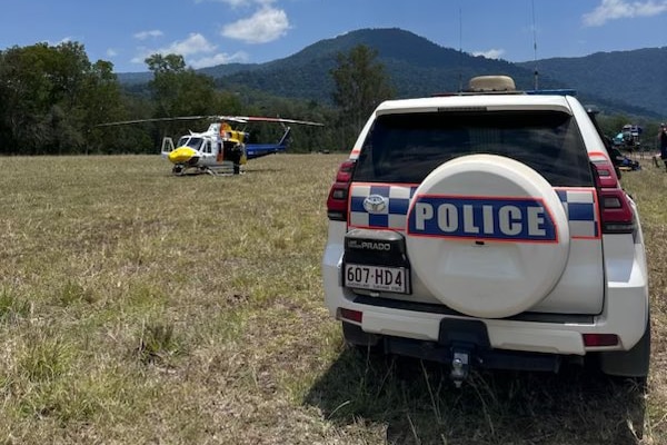 A police car and a CQ rescue helicopter in an open field with trees and mountains visible in background