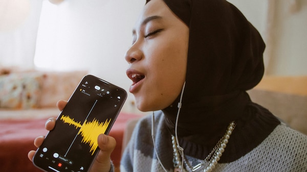 A woman in a colourful jumper and black headscarf singing into her phone.