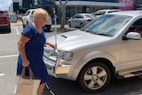 An el;derly woman in a blue summer dress walks to a car.