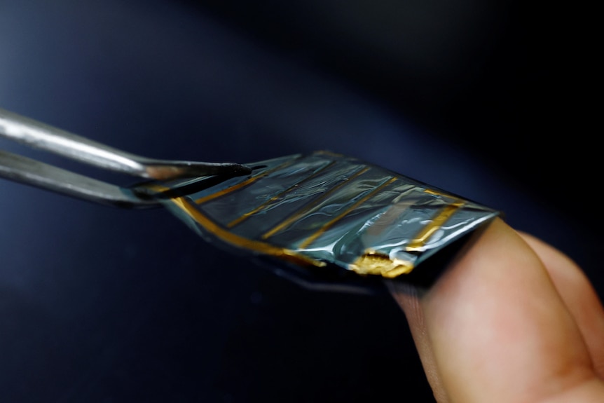 Tweezers hold  piece of reflective metal foil. 