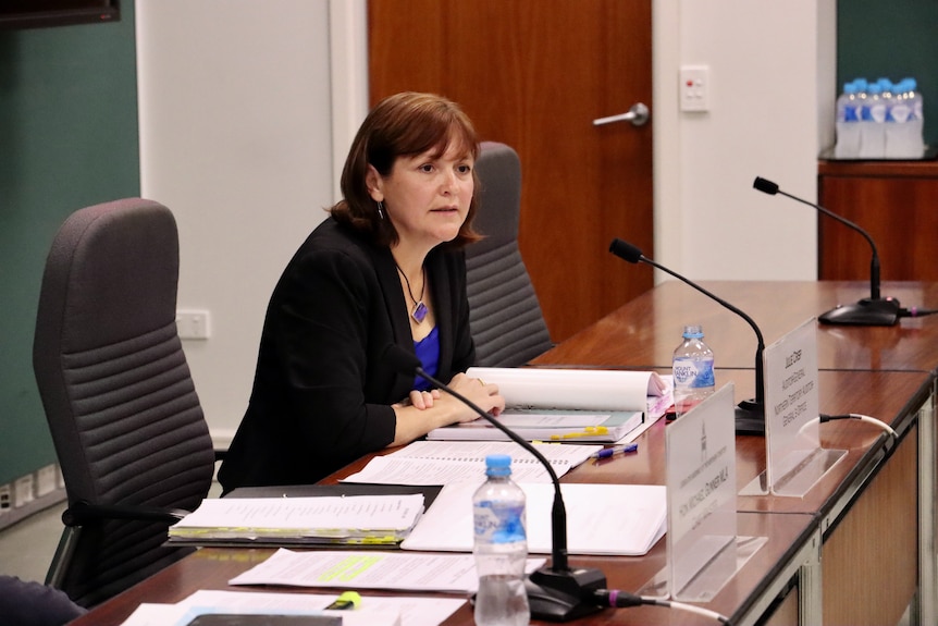 NT Auditor General Julie Crisp speaking into a microphone while sitting at a bench inside a room in parliament. 