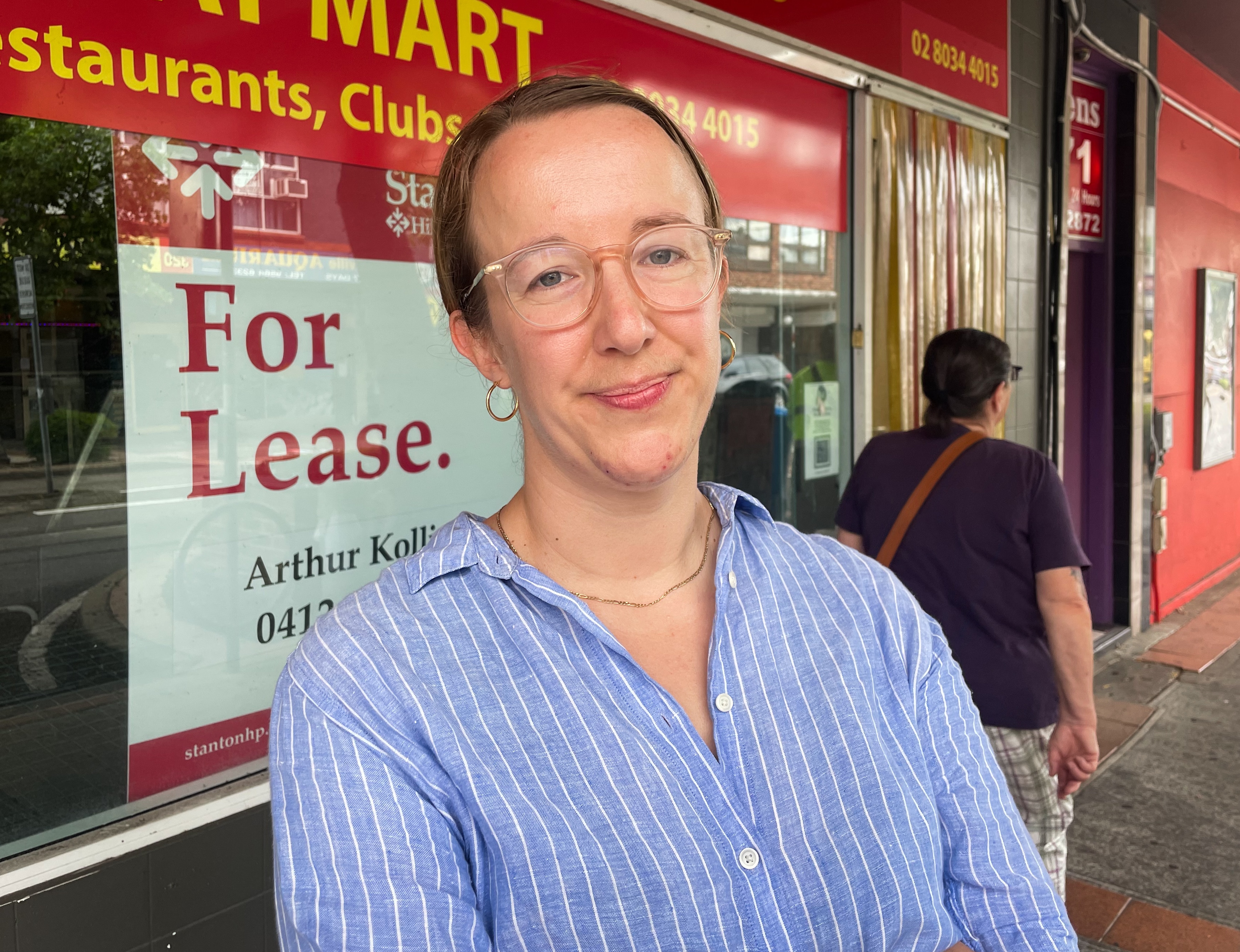 A woman wearing glasses stood in front of a shop window