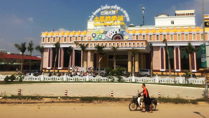 A man pushes a motorbike past a casino in Bavet in Cambodia.