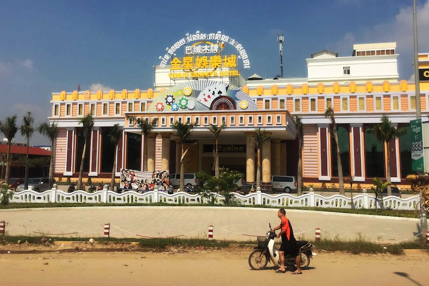 A man pushes a motorbike past a casino in Bavet in Cambodia.