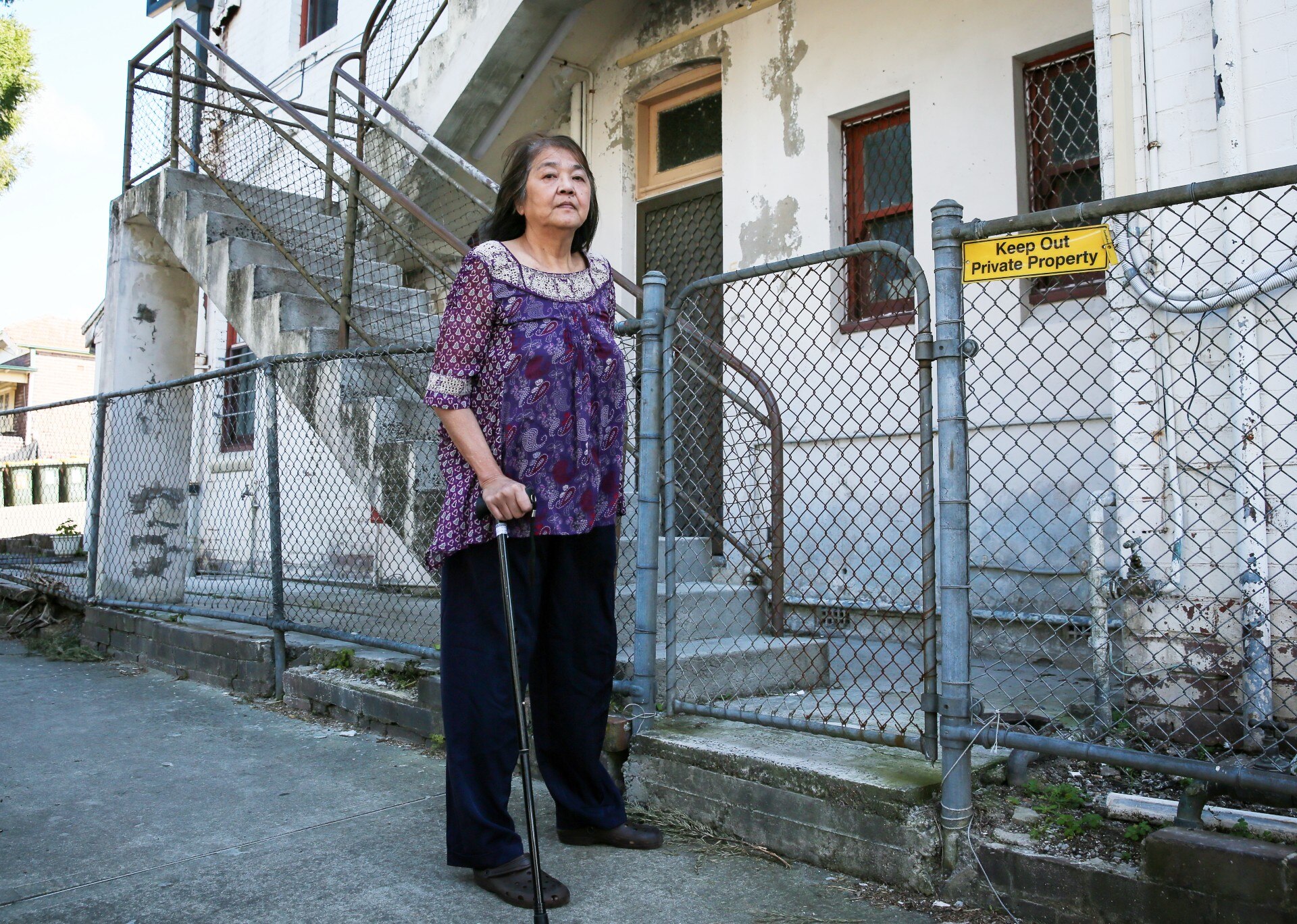 A woman with a walking stick outside a house