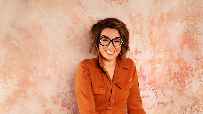 Alice Zaslavsky, smiling, standing in front of a peach-coloured wall.
