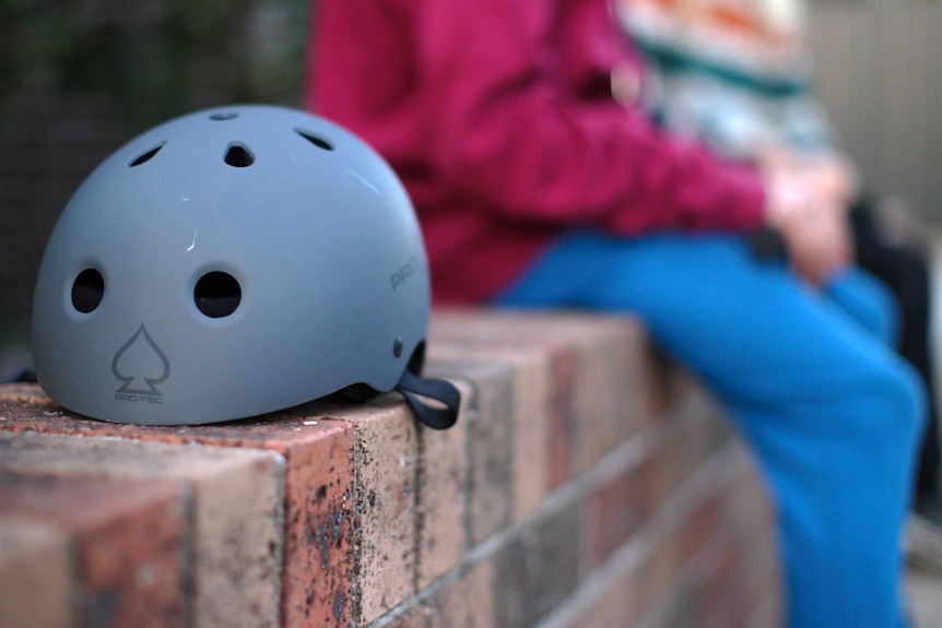 Two unidentifiable children sit on a brick wall. In focus in the foreground is a bike helmet.