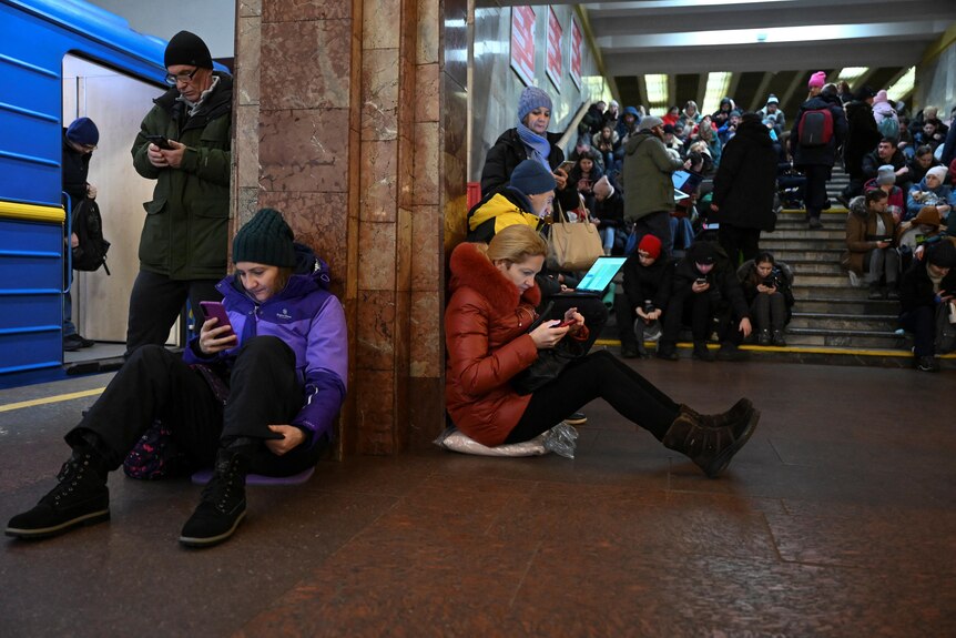People take shelter at a Kyiv metro station, sitting on the floor and on steps.