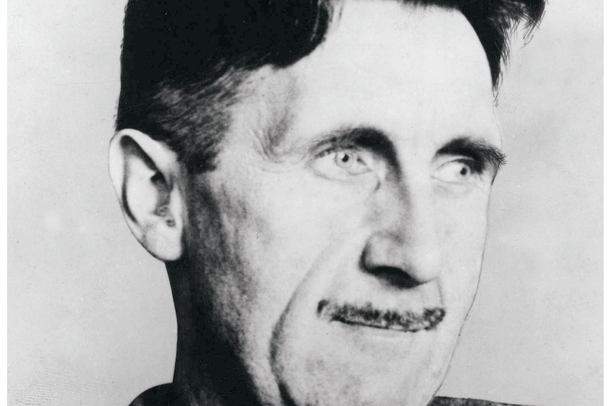 Black and white photo of close-up of George Orwell, very slightly smiling, as he looks off to right. He has a thin moustache.