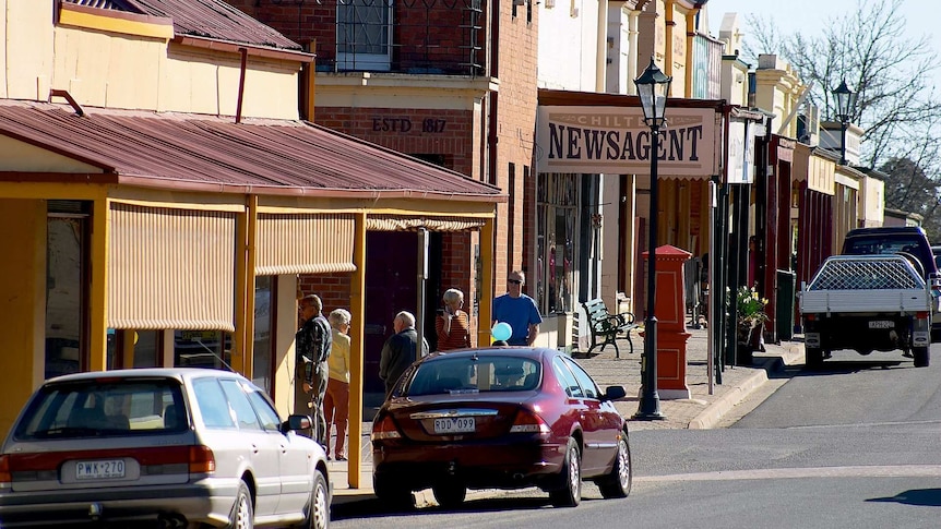 a street of a regional town down with shops, people and cars