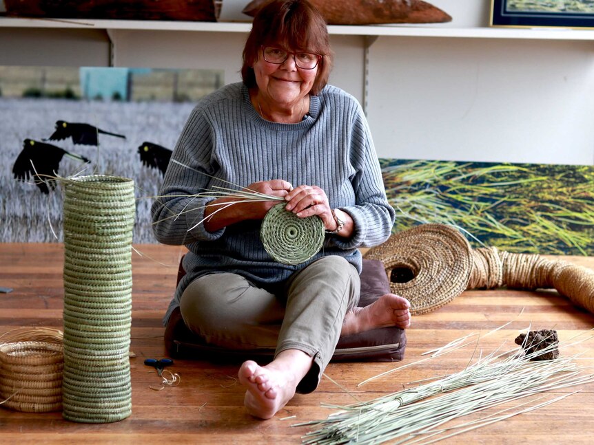 A woman sits on the floor weaving baskets with native grass