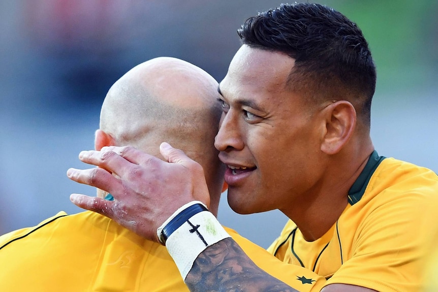 Israel Folau hugs Stephen Moore and pats the back of his head with a cross drawn on his wrist taping