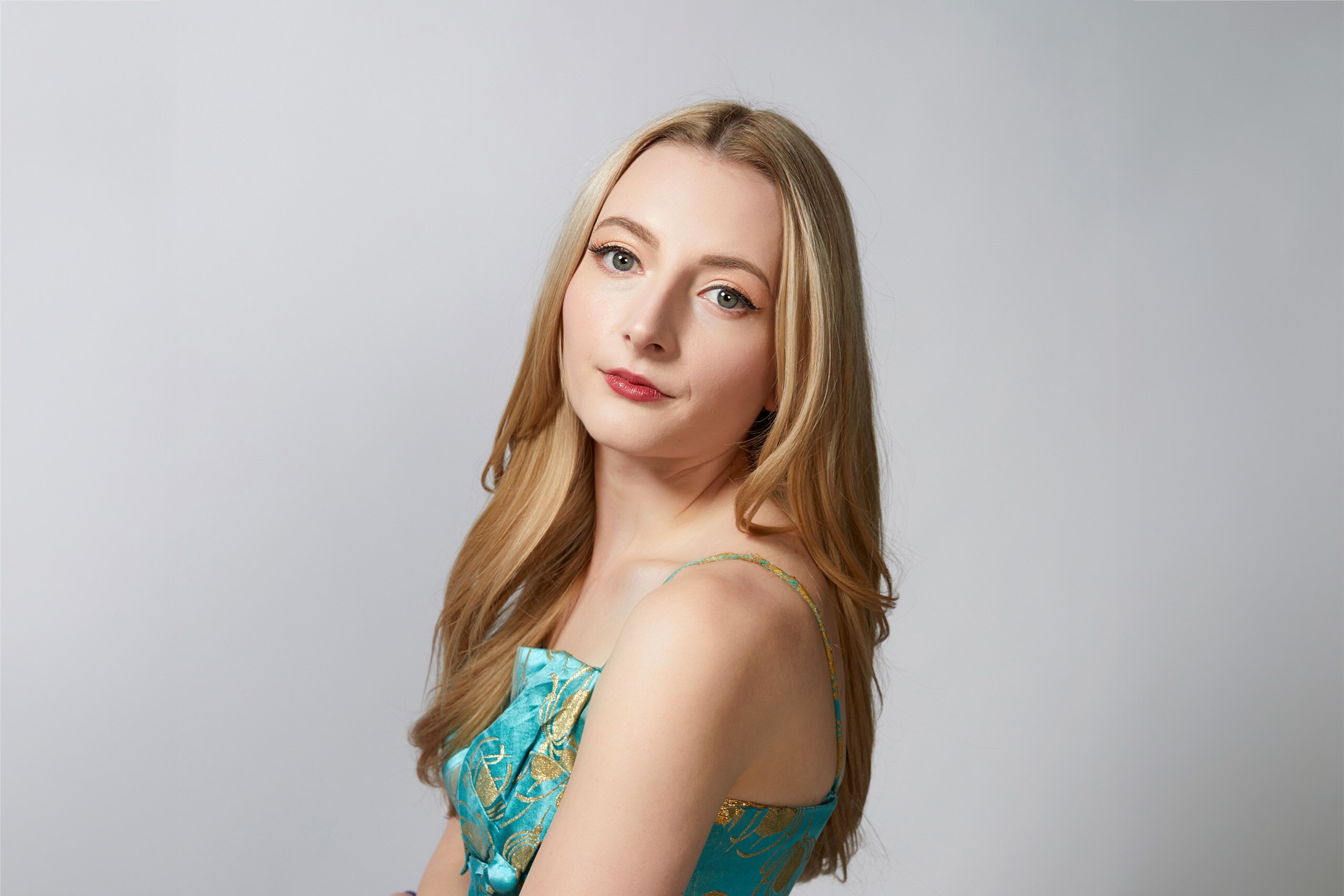 Singer Caity Gyorgy wears a blue dress with golf leaf while looking over her shoulder toward the camera