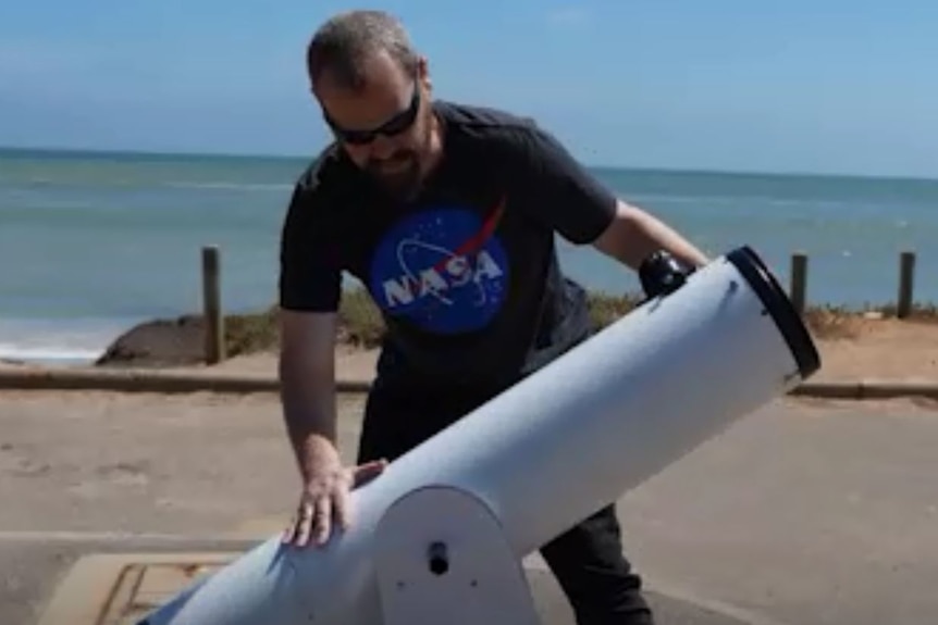 A man, wearing a NASA t-shirt, gets his telescope ready