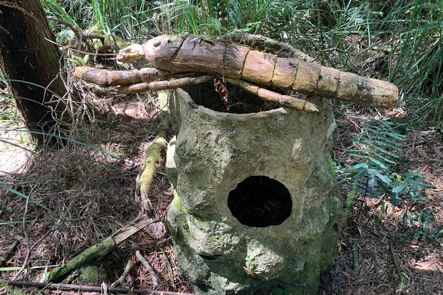 An art installation with a crayfish and stump in woodlands.