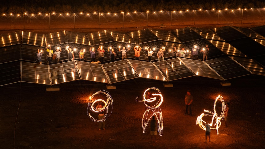 A group of people standing around solar panels at night, with lights and sparklers.
