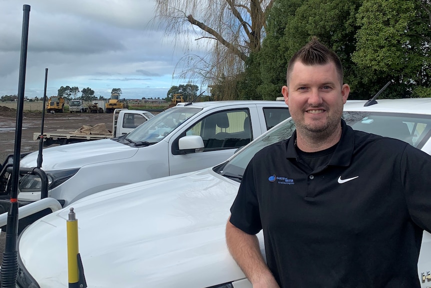 A man in a polo shirt stands in front of a vehicle on a worksite.