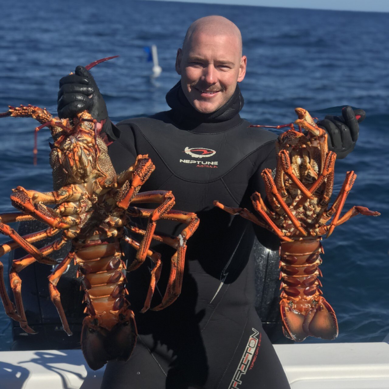 A man in a wet-suit on a boat holding two shell-fish