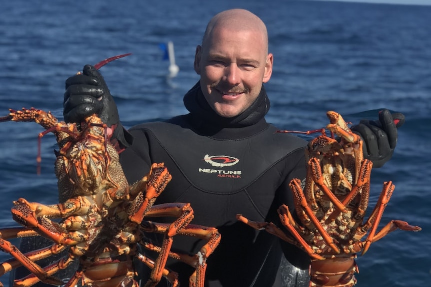 A smiling man in a wetsuit holds up a pair of crustaceans.