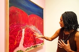 A woman points to a painting hanging on a wall